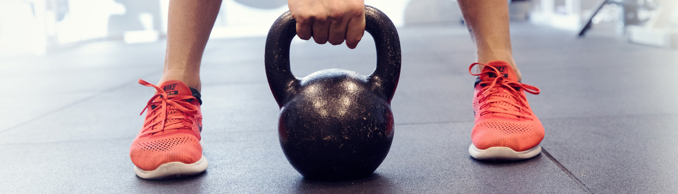 En golvnära bild där en person med oranga skor tar tag i en kettlebell