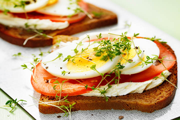 Två mackor med cream cheese, tomat, stekt ägg och lite grönt på toppen.